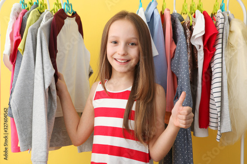 Cute cheerful little girl chooses clothes with floor hangers. Children's clothing, children's shopping. Fashionable clothes for children.