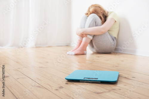 sad teenager girl with scale on wooden floor