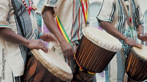 African drummers in ethnic clothes playing on djembe drum close up. Musician beats rhythm on african drums. Black artists hit the drums with their hands