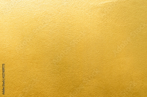Gold wall texture background. Yellow shiny gold foil paint on wall surface with light reflection photo