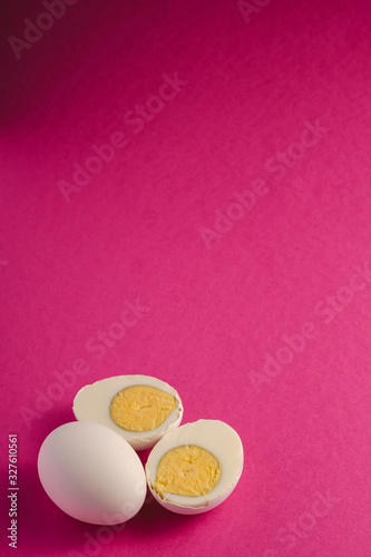 Boiled egg with yellow yolk near to white eggs on vibrant purple pink plain minimal background, angle view, happy Easter day, copy space