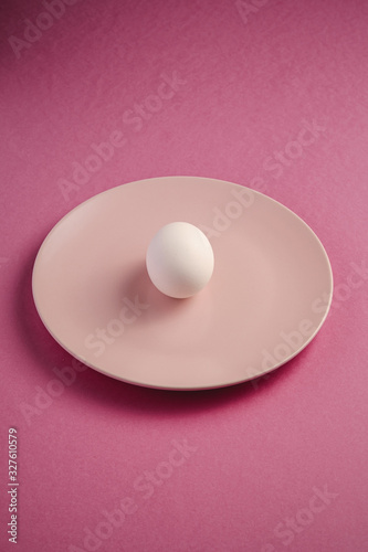 White egg in pink plate on purple plain minimal background, angle view, happy Easter day