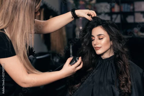 Fototapeta na wymiar Female hairdresser makes hairstyle on young woman with brunette hair in salon.