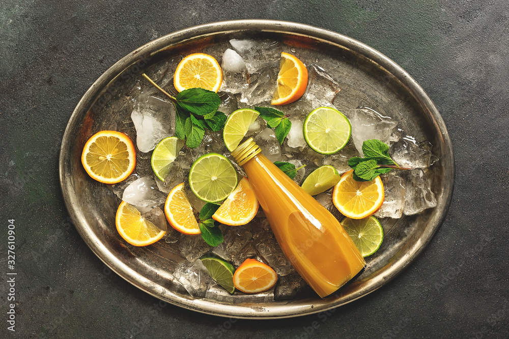 Orange juice with pulp in a bottle, slices of citrus and crushed ice on a vintage metal tray. Top view, flat lay. Orange juice with pulp in a bottle, slices of citrus and crushed ice on a vintage metal tray. Top view, flat lay.