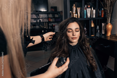 Foto Female hairdresser makes hairstyle on young woman with brunette hair in salon