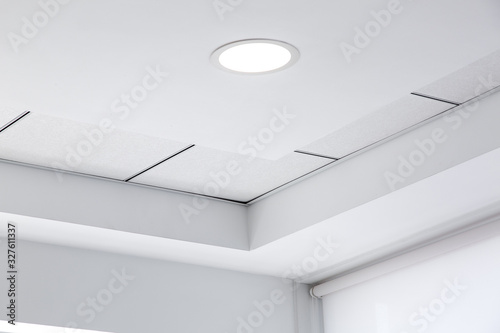 multi-level ceiling with three-dimensional protrusions and a suspended tiled ceiling with a built-in round led light in the corner of the room, close up details. photo