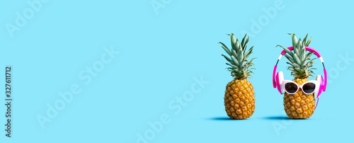 Pineapple wearing headphones with regular pineapple on a solid background