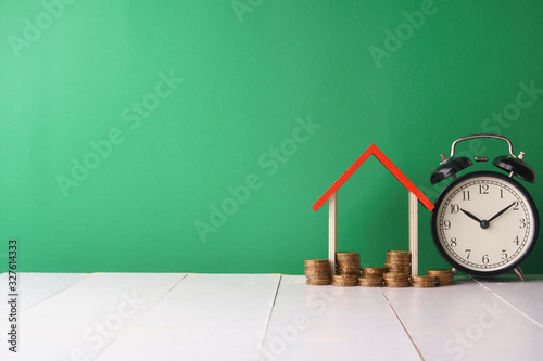 business and finance management conceptual images. stacked money, home replica and clock against green background. copy space for your text