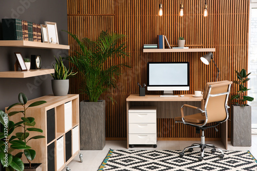 Comfortable workplace with computer near wooden wall in stylish room interior. Home office design