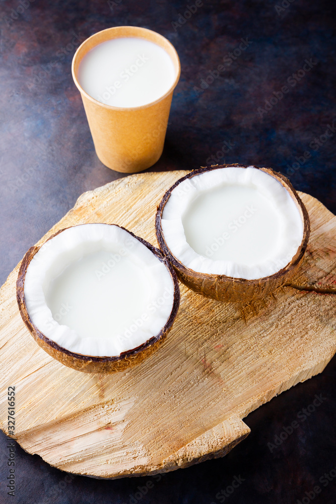 Coconut milk and coconut in paper glass on dark background. Coconut vegan milk non dairy on a wooden stand. Healthy drink concept. Alternative milk. Top view Coconut milk and coconut in paper glass on dark background. Coconut vegan milk non dairy on a wooden stand. Healthy drink concept. Alternative milk. Top view