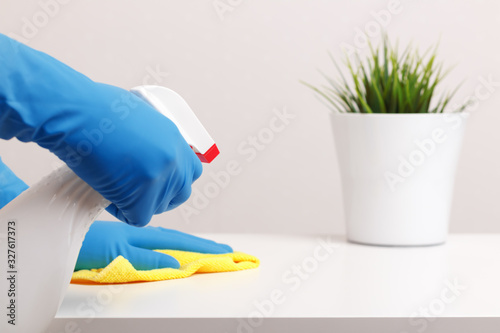 Close up of female hands in protective rubber gloves, napkin and spray. Cleaning the desktop in the room
