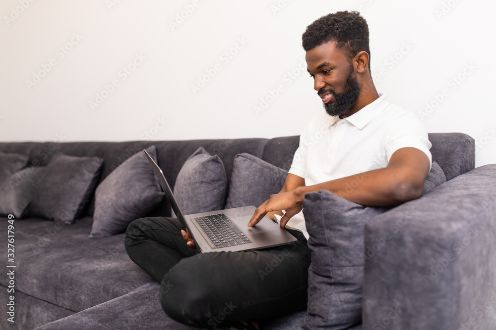 Happy smiling african man watching and working on computer laptop at home