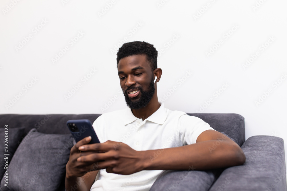 Handsome african man making a phone call via airpods while sitting on a couch in his living room Handsome african man making a phone call via airpods while sitting on a couch in his living room