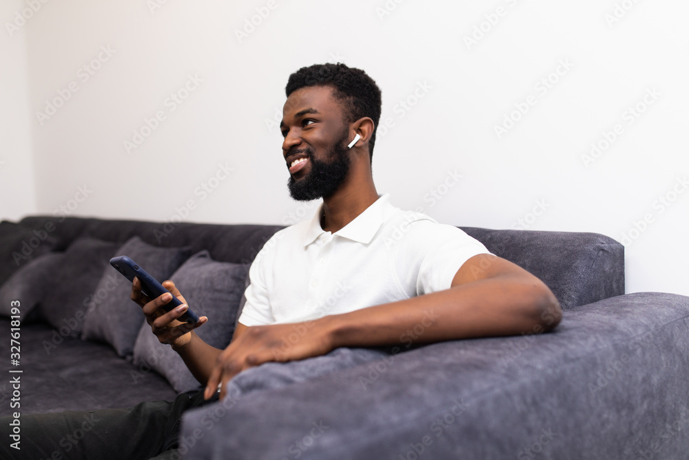 Handsome african man making a phone call via airpods while sitting on a couch in his living room Handsome african man making a phone call via airpods while sitting on a couch in his living room