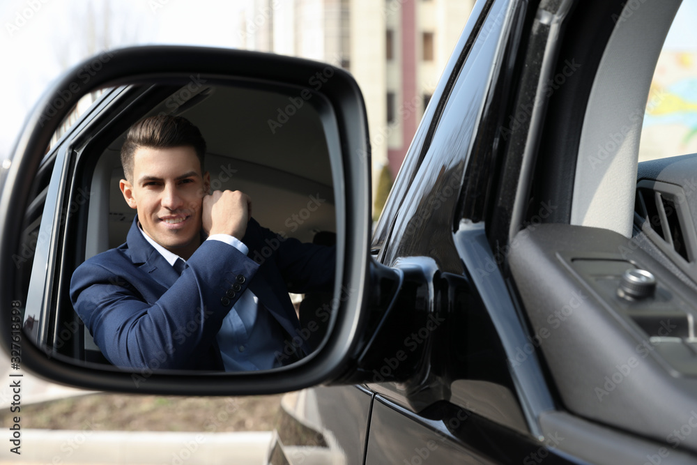 Handsome man looking into side view mirror of modern car outdoors