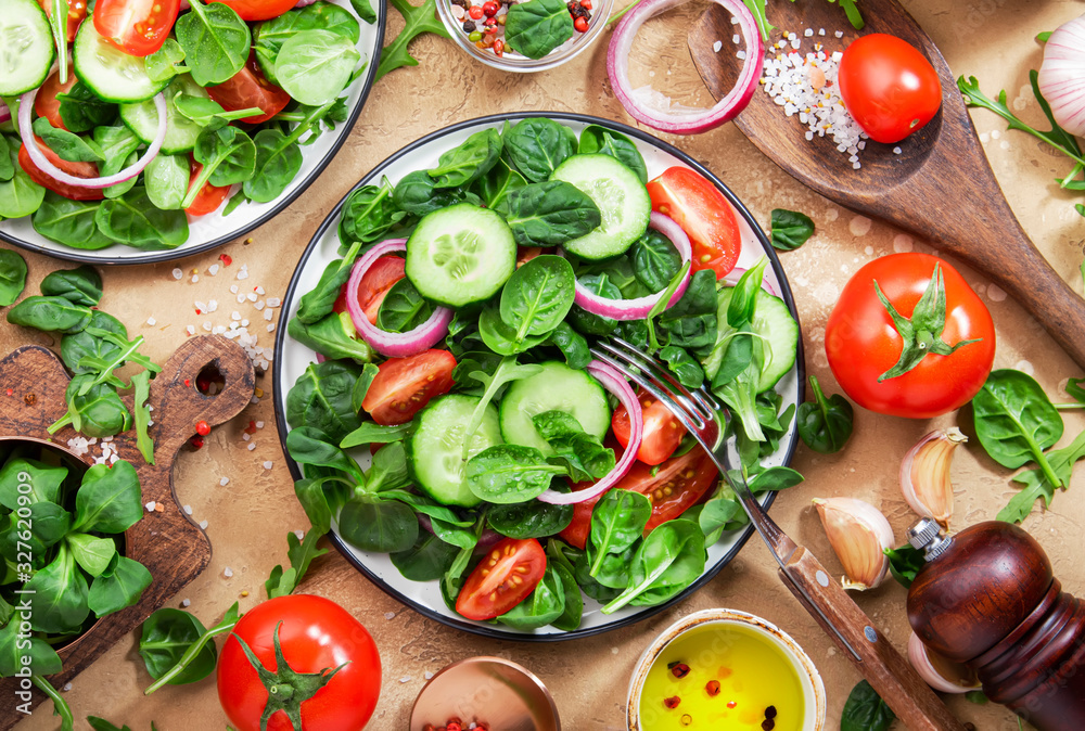 Spring vegan salad with spinach, cherry tomatoes, corn salad and red onion. Healthy food concept. Beige stone table background. Top view Spring vegan salad with spinach, cherry tomatoes, corn salad and red onion. Healthy food concept. Beige stone table background. Top view