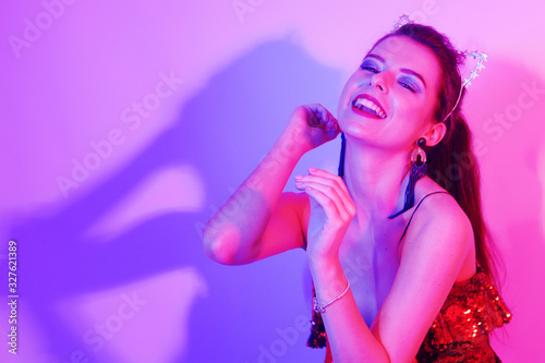 Gorgeous girl dancing in a neon light. A girl in a red shiny dress and with cat ears is dancing