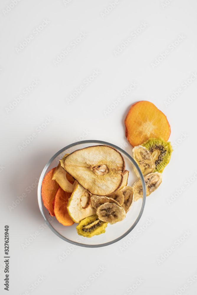 Healthy snack. Homemade dehydrated chips of apple, kiwi, banana, persimmon, pear in a glass dish on a white background. Dietary nutrition.