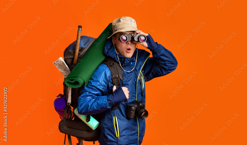 Amazed backpacker using binoculars, orange studio background