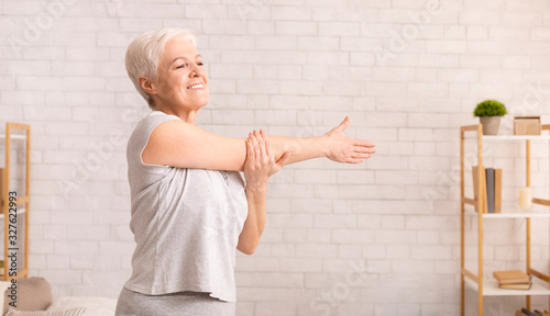 Positive senior lady warming up her hands at home photo