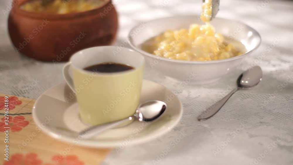 Rack focus Cup of coffee in the foreground with spoon placing mungunzá on a plate in the background. Rack focus Cup of coffee in the foreground with spoon placing mungunzá on a plate in the background.