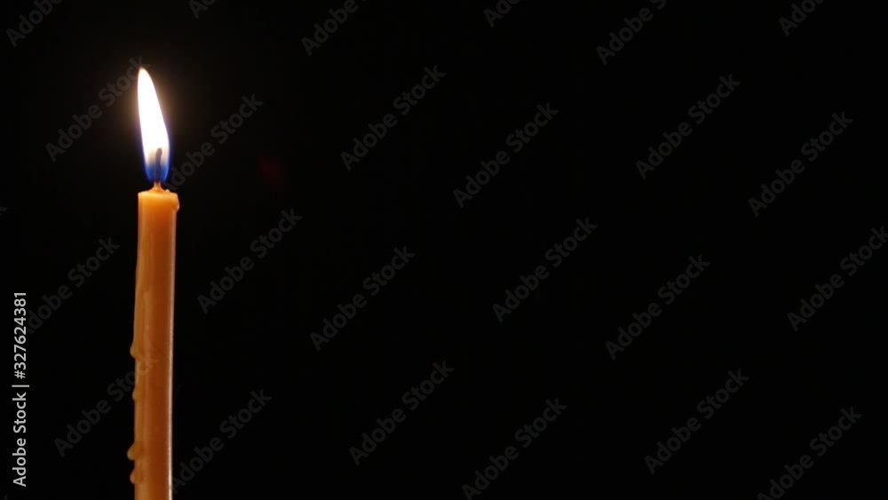 A candle is lit with a match. A long wax candle burns at the edge of the frame on a black background. Space reserved for captions. Flames occasionally sway from the movement of air.