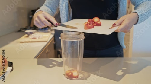 A woman scraps strawberries from a chopping board into a blender in order to make a fruit smoothie for breakfast.  photo
