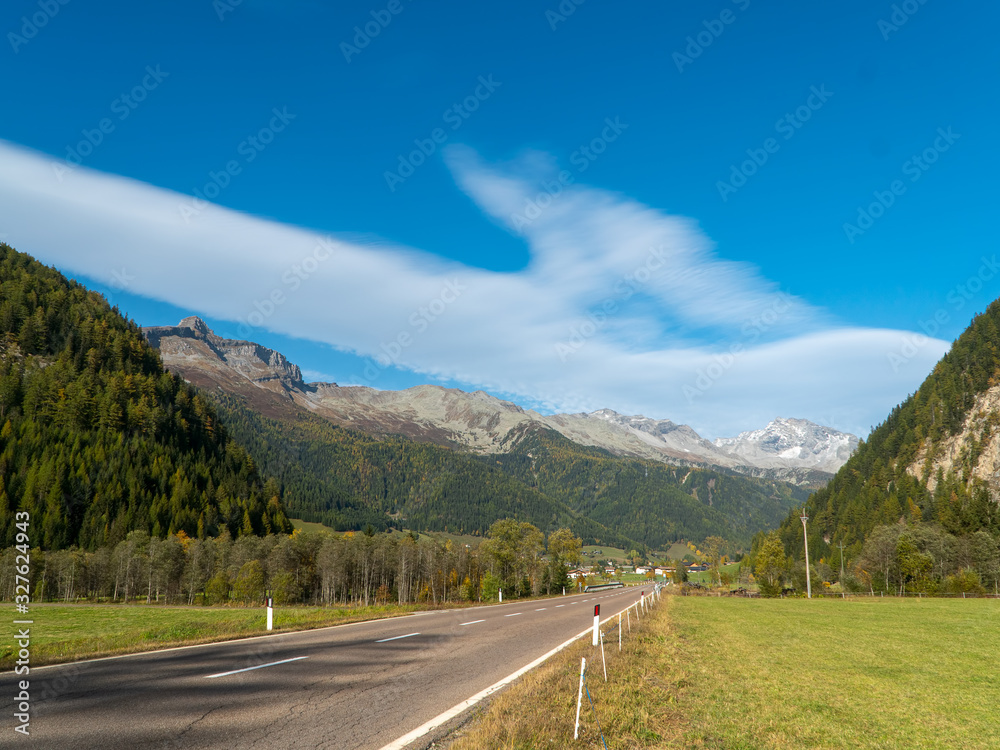 Direct rural asphalt road in the Alpine mountains valley in autumn, blue sky background