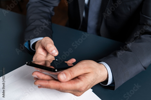 A businessman in suit typing on smartphone. Formal wearing.