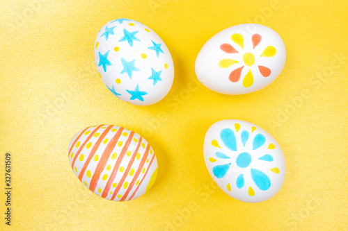 Easter concept. White eggs with marker simple children's drawings. Manual coloring. Yellow, blue and red shades. Golden background. Flat lay, top view, copyspace.