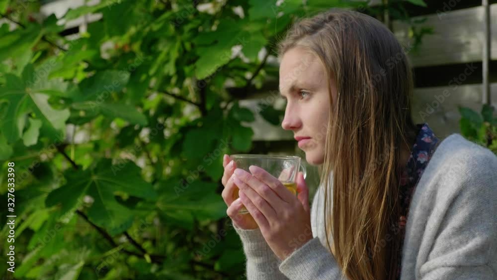Girl with long hair sits outside enjoying tea and staring out, medium Girl with long hair sits outside enjoying tea and staring out, medium