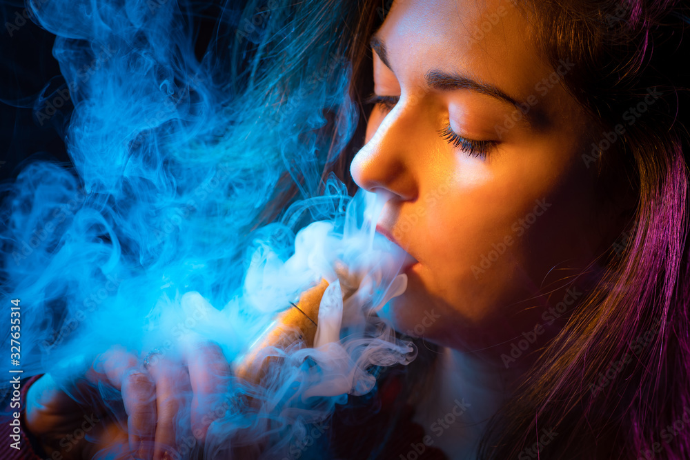 Girl in the dark is engaged in vaping. Woman face with electronic cigarette  close up. Student