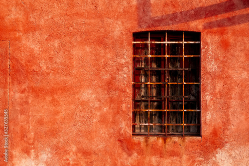 Vecchia finestra con balconi chiusi e sbarre su muro rosso di casa abbandonata.