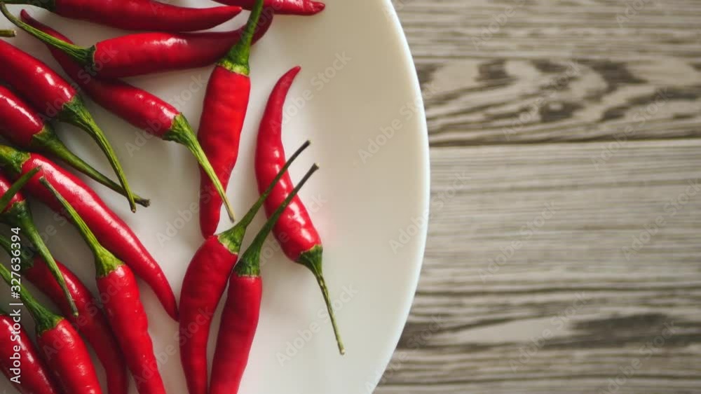 Top View Of Fresh Raw Red Chili Peppers Rotating On A White Plate On A Gray Wooden Background On The Left Side.