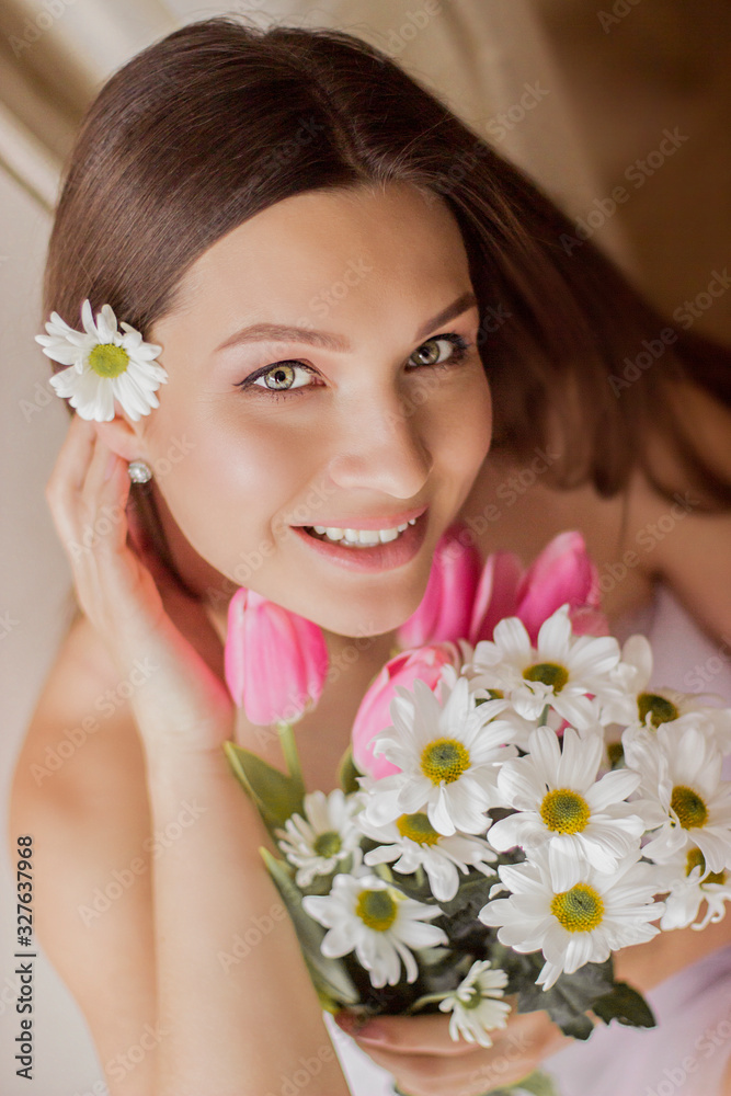 Portrait of young beautiful woman holding flowers in hand and smiling. Closeup of tender happy girl posing with bouquet of tulips and daisies. Naked girl celebrating 8 march, women's or mother's day