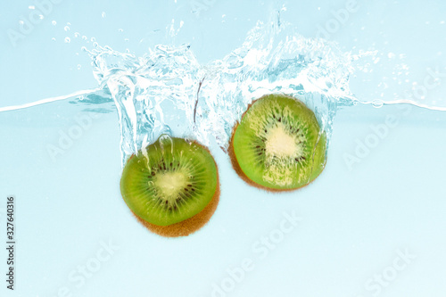 Fresh kiwi halves dropping into clear water with splashes on blue background