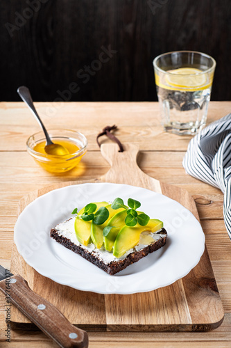 Open sandwich with cream cheese, sliced avocado and lamb's lettuse on a wooden cutting board photo