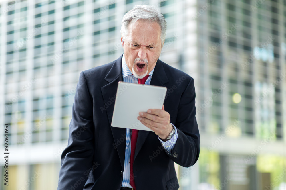 Senior manager looking anrgy because he reads bad news on his tablet Senior manager looking anrgy because he reads bad news on his tablet