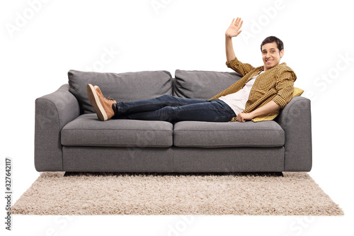 Guy in casual clothes resting on a sofa and waving at the camera