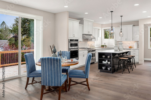 Kitchen and dining area in new luxury home. Features kitchen island, table with place settings, stainless steel appliances, and pendant lights.