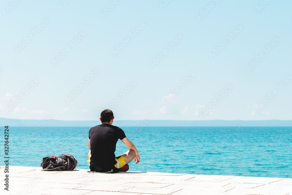man traveler backpacker sitting on the seashore looking into the ocean