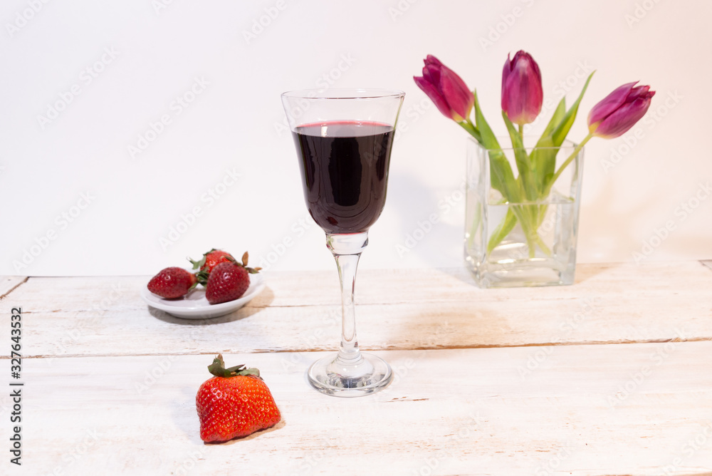glass of red wine, red berry, strawberry on plate, pink tulips in vase on white background glass of red wine, red berry, strawberry on plate, pink tulips in vase on white background