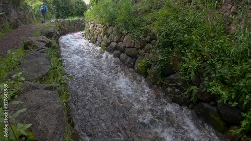 Tourists walking along a path surrounded by a lot of vegetation next to a clear water stream in the sacred valley of the incas, located in Cusco, Perú. photo