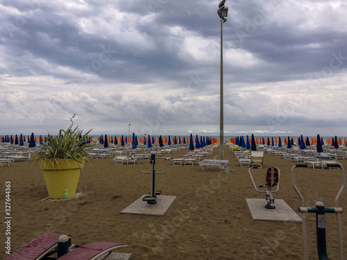 View of an empty sandy beach in cloudy weather with umbrellas folded and lying