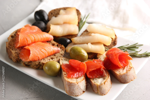 Snack. Bread slices with red and white fish. Olives and rosemary on a white plate. Smoked fish. Black bread and baguette. Background image, copy space