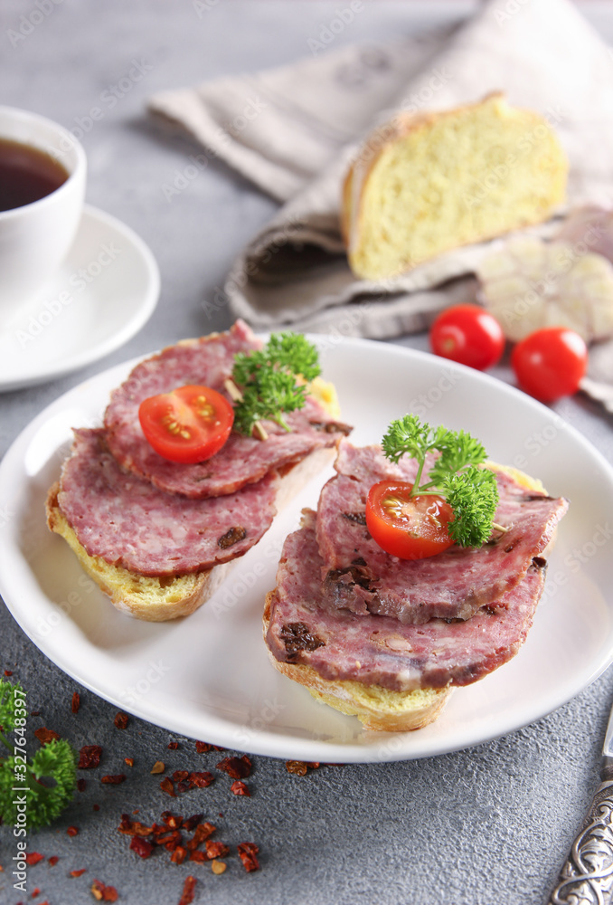 Lunch. Sandwiches with sausage and a cup of coffee on a light grey background. Tomatoes, garlic, white bread, parsley, knife and spices. Background image, copy space