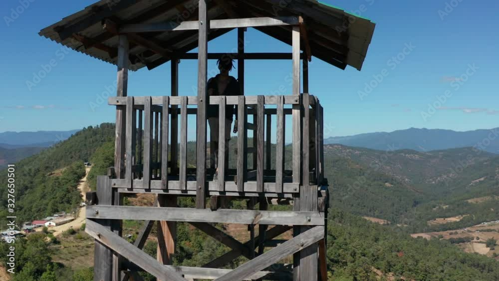 Man climbs a wooden lookout tower in wilderness, close aerial rise up Man climbs a wooden lookout tower in wilderness, close aerial rise up