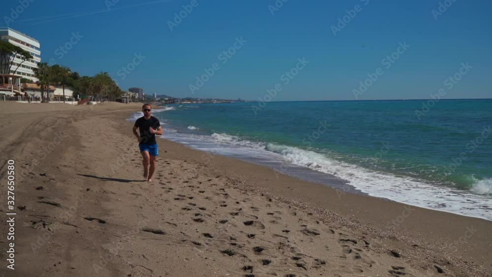 Caucasian man running along the beach seen ahead Caucasian man running along the beach seen ahead