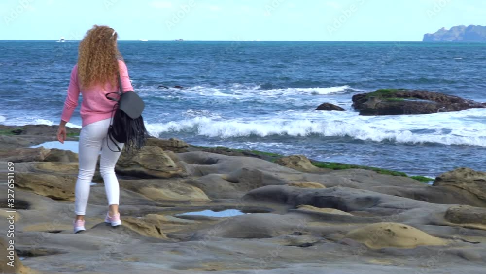 beautiful curly girl on the volcanic shore in bright casual clothes on a sunny day. blond hair develops in the wind. a girl in pink walks on an unusual shape of the ocean in Taiwan. rock elephant beautiful curly girl on the volcanic shore in bright casual clothes on a sunny day. blond hair develops in the wind. a girl in pink walks on an unusual shape of the ocean in Taiwan. rock elephant