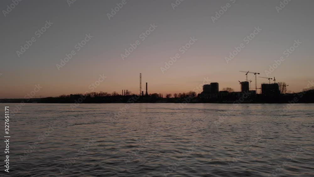Push in drone flying video over a river as cranes constructing industrial buildings, nuclear power plants at sunset. Push in drone flying video over a river as cranes constructing industrial buildings, nuclear power plants at sunset.
